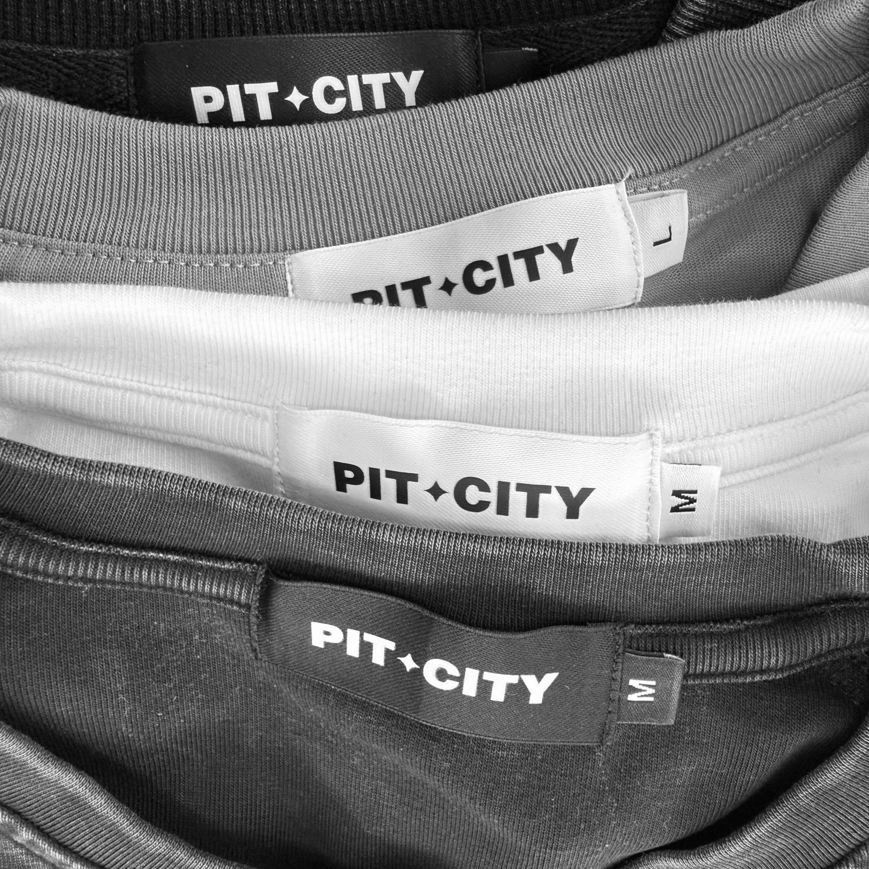 Pit City apparel labels sewn into black, white, and grey garments.